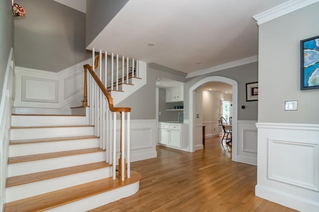 stairs featuring arched walkways, ornamental molding, wood finished floors, and a decorative wall