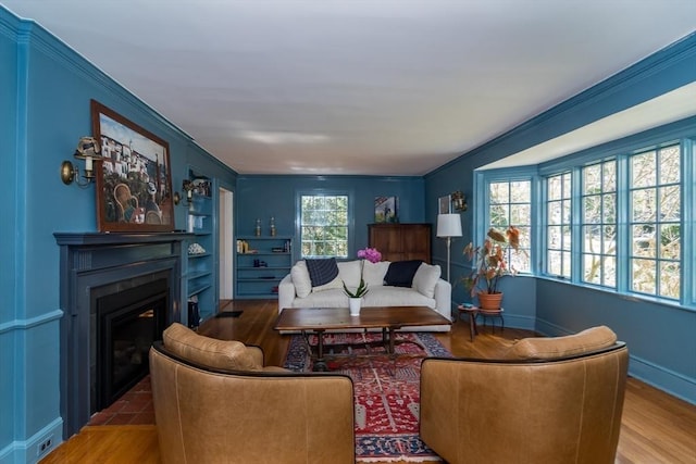 living room with baseboards, wood finished floors, crown molding, and a glass covered fireplace