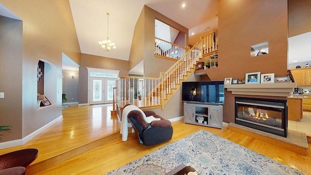 living area with a high ceiling, light wood-type flooring, a chandelier, a multi sided fireplace, and stairs