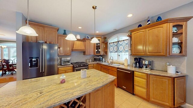 kitchen with appliances with stainless steel finishes, light stone counters, a sink, glass insert cabinets, and tasteful backsplash