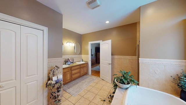 bathroom with a wainscoted wall, a freestanding tub, vanity, tile patterned flooring, and tile walls