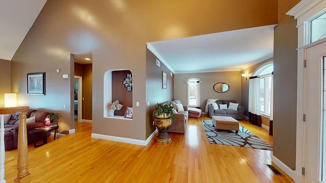 living area with arched walkways, light wood-style flooring, plenty of natural light, baseboards, and a towering ceiling