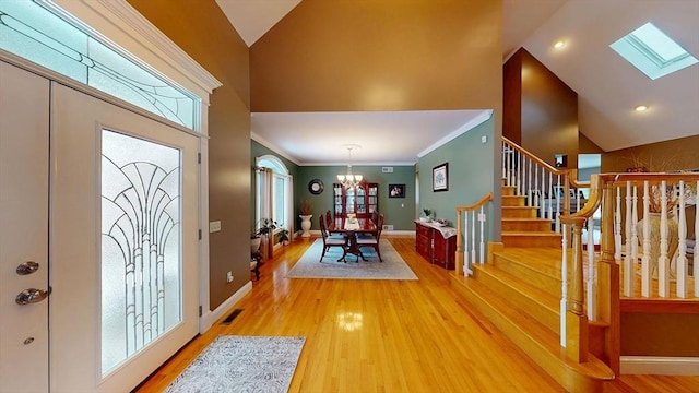 foyer entrance featuring light wood-style flooring, healthy amount of natural light, a chandelier, ornamental molding, and high vaulted ceiling