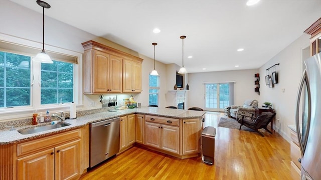 kitchen featuring a peninsula, appliances with stainless steel finishes, a sink, and light wood-style flooring