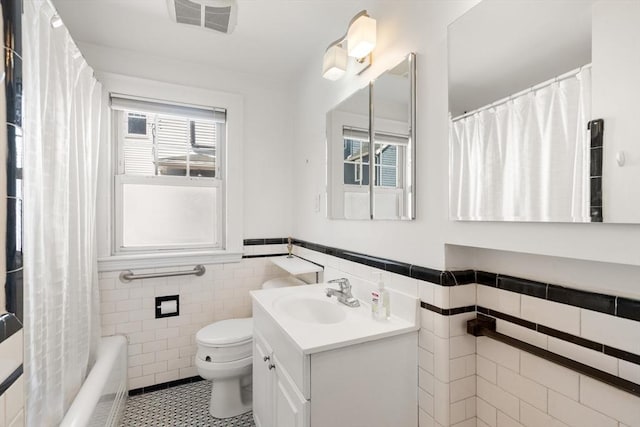 bathroom featuring visible vents, vanity, wainscoting, toilet, and tile walls