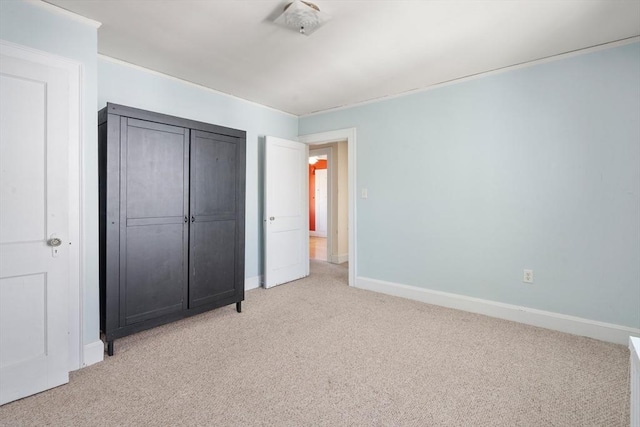 unfurnished bedroom featuring baseboards, light colored carpet, and a closet