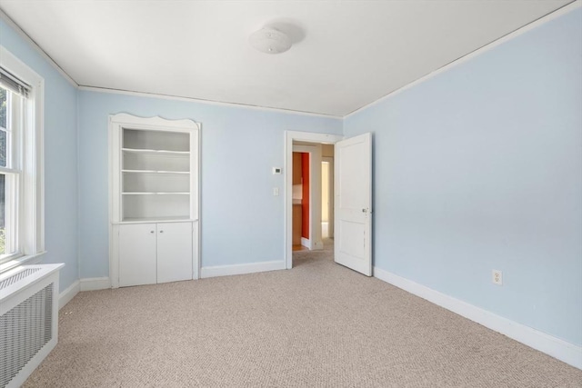 unfurnished bedroom with baseboards, light carpet, and radiator