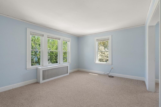 empty room featuring baseboards, radiator, a healthy amount of sunlight, and light carpet
