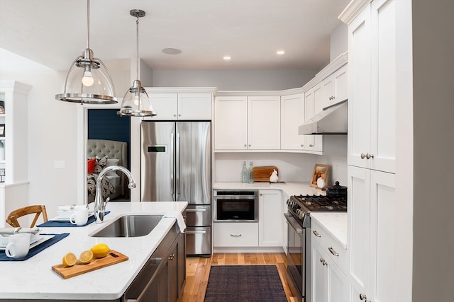 kitchen with pendant lighting, appliances with stainless steel finishes, sink, white cabinetry, and light stone countertops