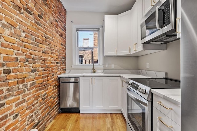 16 Foster St Unit 5, Boston, MA 02109 - kitchen with stainless steel appliances, brick wall, light wood finished floors, light countertops, and white cabinetry