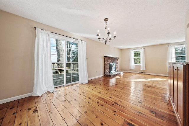 unfurnished living room featuring light wood finished floors, baseboards, visible vents, a fireplace, and a chandelier