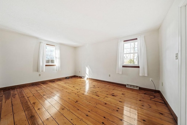 spare room with a healthy amount of sunlight, wood-type flooring, visible vents, and baseboards