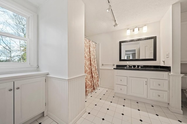 bathroom featuring a wainscoted wall, rail lighting, a textured ceiling, vanity, and a shower with curtain