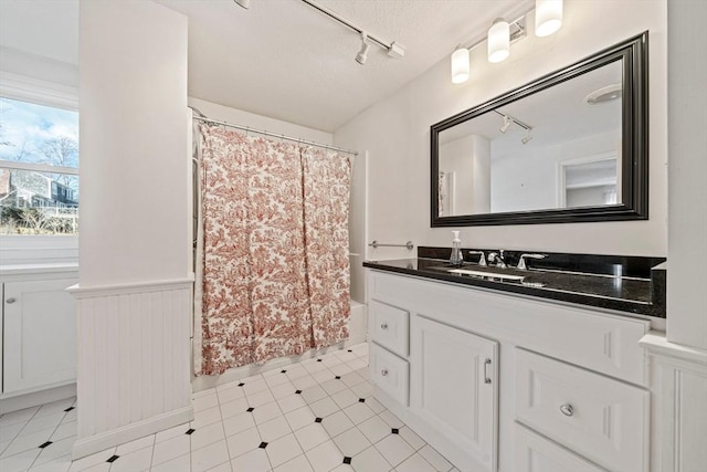 full bathroom featuring a textured ceiling, a wainscoted wall, vanity, shower / bath combo, and rail lighting