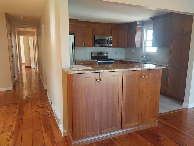 kitchen featuring appliances with stainless steel finishes, backsplash, light wood-style flooring, and a peninsula