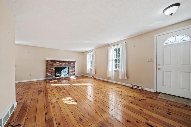 unfurnished living room featuring light wood-type flooring, a brick fireplace, visible vents, and baseboards