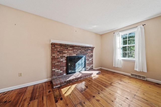 unfurnished living room with baseboards, visible vents, a fireplace, and hardwood / wood-style floors