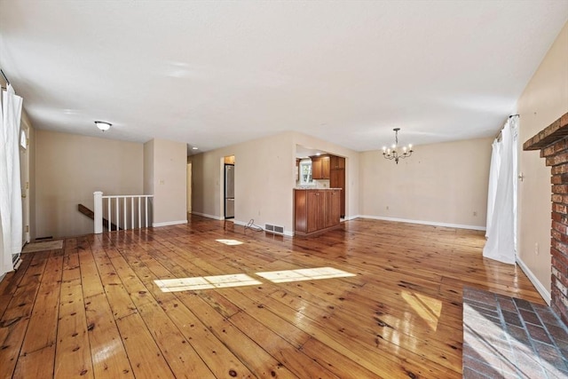 unfurnished living room featuring light wood-type flooring, visible vents, baseboards, and an inviting chandelier