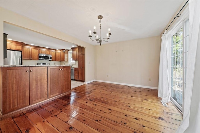 kitchen featuring a chandelier, baseboards, appliances with stainless steel finishes, brown cabinets, and light wood finished floors