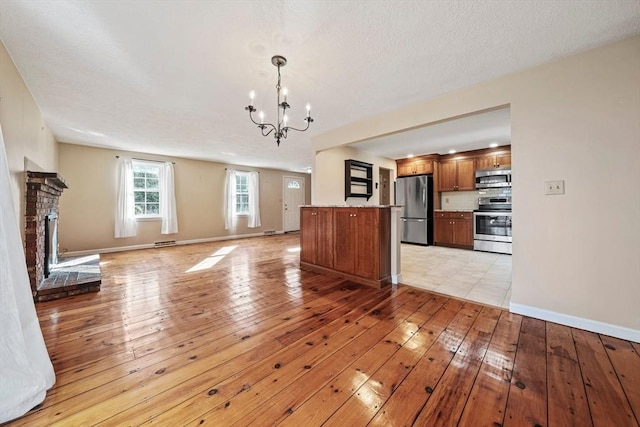 unfurnished living room with baseboards, a brick fireplace, a chandelier, and light wood-style floors