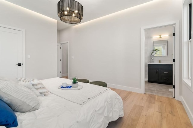 bedroom with connected bathroom, sink, and light hardwood / wood-style floors