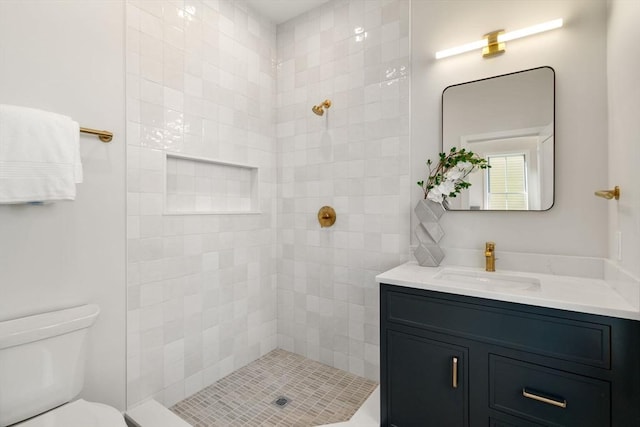 bathroom featuring a tile shower, vanity, and toilet