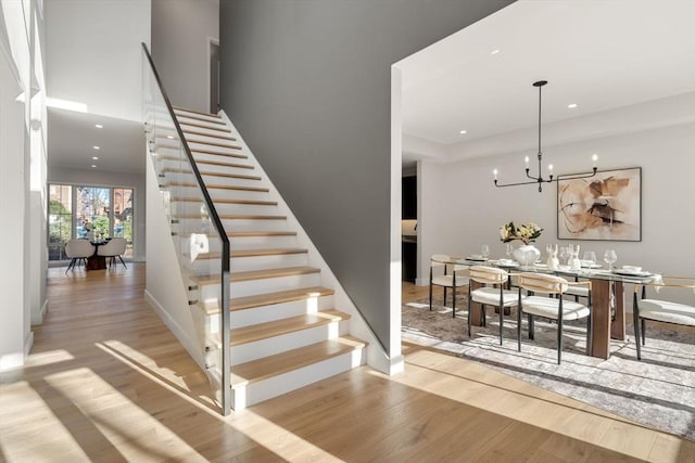 stairs featuring wood-type flooring and an inviting chandelier