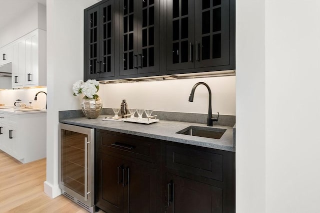 bar featuring light hardwood / wood-style flooring, white cabinets, beverage cooler, and sink