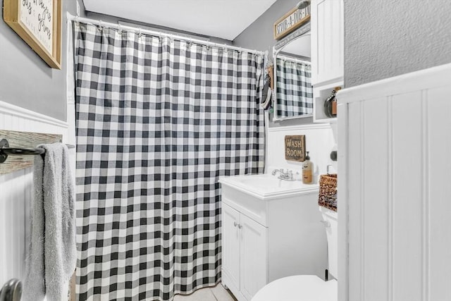 full bath with a shower with shower curtain, vanity, toilet, and wainscoting