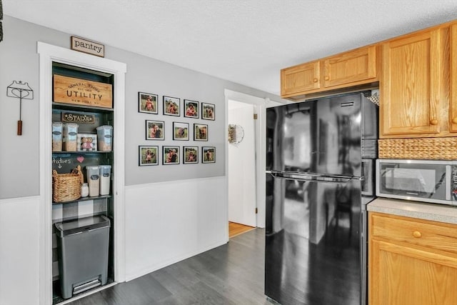 kitchen featuring dark wood finished floors, stainless steel microwave, freestanding refrigerator, light countertops, and a textured ceiling