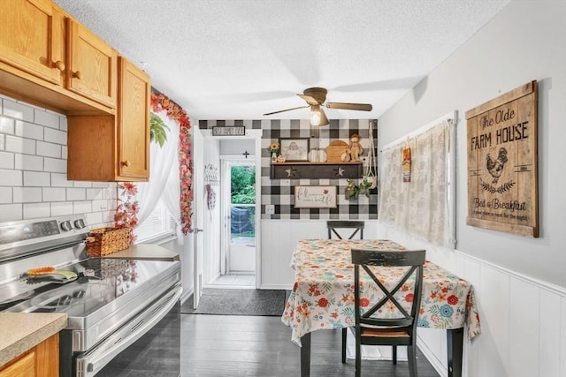 kitchen featuring stainless steel range with electric stovetop, a textured ceiling, a wainscoted wall, and wood finished floors