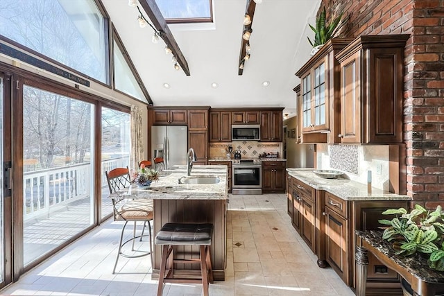 kitchen featuring tasteful backsplash, light stone counters, stainless steel appliances, sink, and a center island with sink