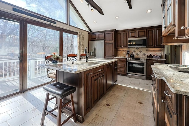 kitchen featuring sink, stainless steel appliances, light stone counters, an island with sink, and vaulted ceiling