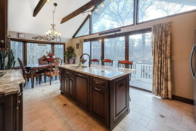 kitchen with light stone counters, sink, beam ceiling, hanging light fixtures, and an island with sink