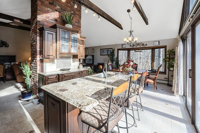 kitchen with sink, light stone counters, beamed ceiling, backsplash, and a chandelier