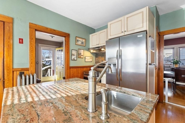 kitchen featuring sink, wood walls, stainless steel fridge with ice dispenser, dark hardwood / wood-style floors, and light stone countertops