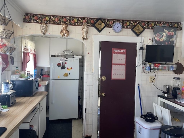 kitchen with black microwave, freestanding refrigerator, and tile walls