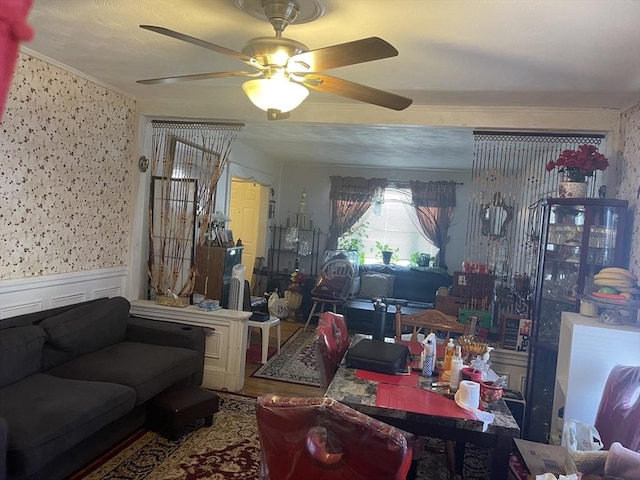 living room featuring ornamental molding, a ceiling fan, wainscoting, and wood finished floors