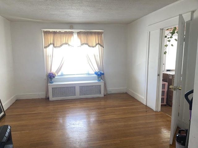 unfurnished dining area with radiator, a textured ceiling, baseboards, and wood finished floors