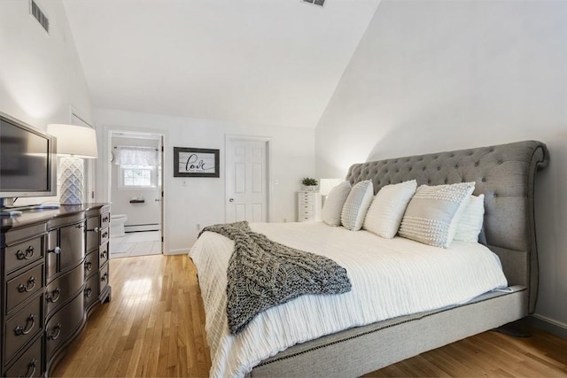 bedroom featuring lofted ceiling, a baseboard heating unit, light wood-type flooring, and ensuite bath