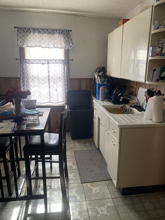 kitchen with a wainscoted wall, light countertops, white cabinets, wooden walls, and a sink