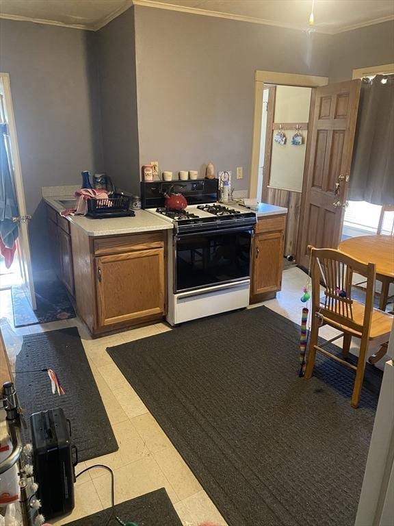 kitchen with range with gas stovetop, crown molding, light countertops, brown cabinets, and healthy amount of natural light