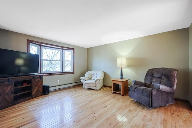 living area with a baseboard heating unit, hardwood / wood-style flooring, and baseboards