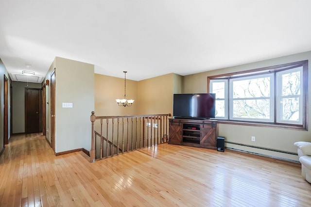 unfurnished living room with a baseboard heating unit, attic access, a notable chandelier, and light wood-type flooring