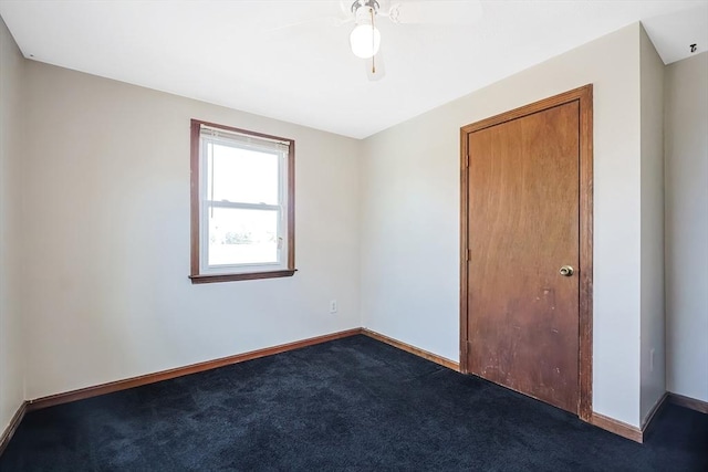 unfurnished room with baseboards, a ceiling fan, and dark carpet