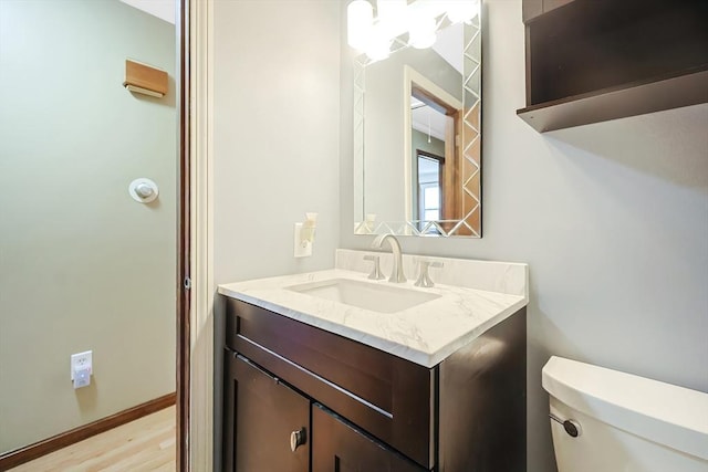 half bathroom with vanity, toilet, wood finished floors, and baseboards