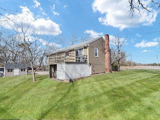 rear view of property featuring an outbuilding, a lawn, a chimney, and a deck