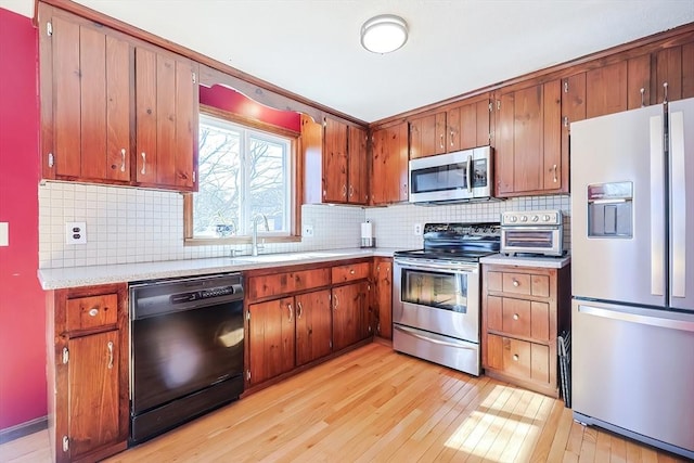 kitchen featuring light wood-style flooring, a sink, stainless steel appliances, light countertops, and backsplash