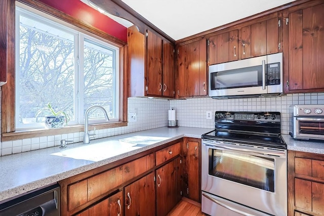 kitchen with a sink, tasteful backsplash, stainless steel appliances, brown cabinetry, and a toaster