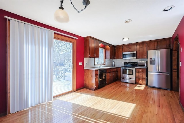 kitchen with a sink, decorative backsplash, light countertops, stainless steel appliances, and light wood-type flooring